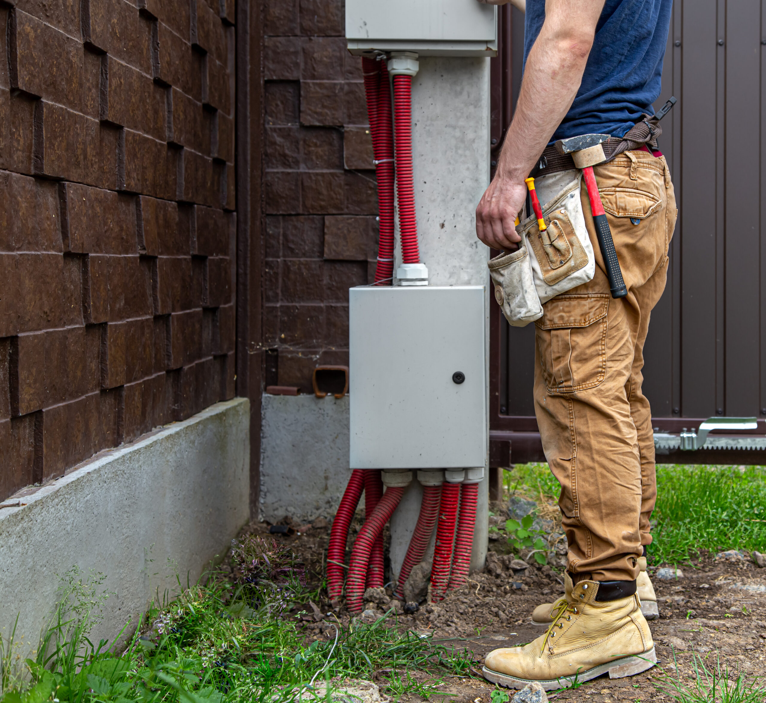 Electrician Builder at work, examines the cable connection in the electrical line in the fuselage of an industrial switchboard. Professional in overalls with an electrician's tool.